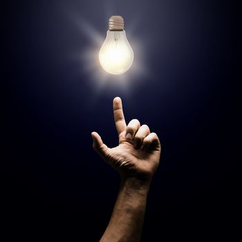 Human hand pointing with finger at electrical bulb