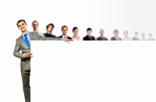 Image of young man holding blank banner with crowd of business people at background