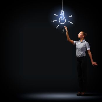 Image of attractive businesswoman against dark background and bulb