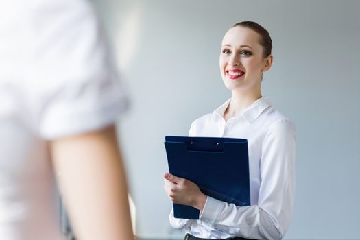 Image of young businesswoman holding folder and talking to colleague