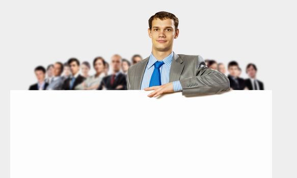 Image of young man holding blank banner with crowd of business people at background