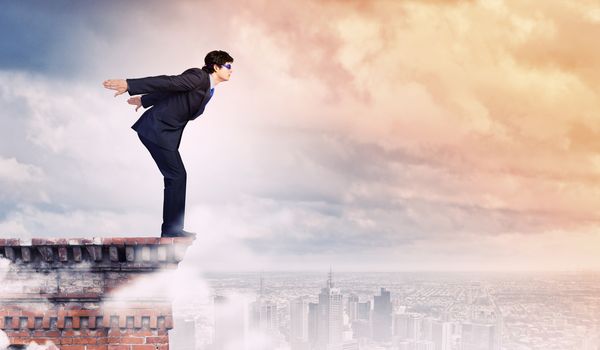 Image of young businessman in goggles jumping from top of building