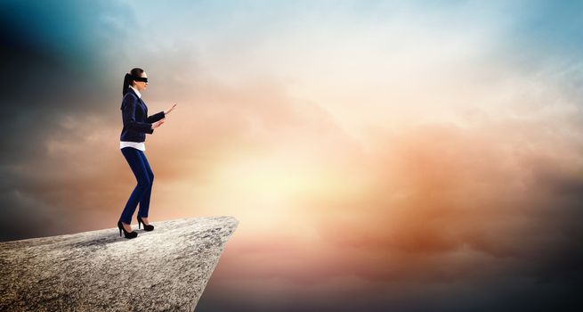 Image of businesswoman in blindfold standing on edge of mountain