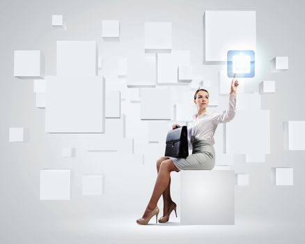 Image of elegant businesswoman sitting on white cube touching media button