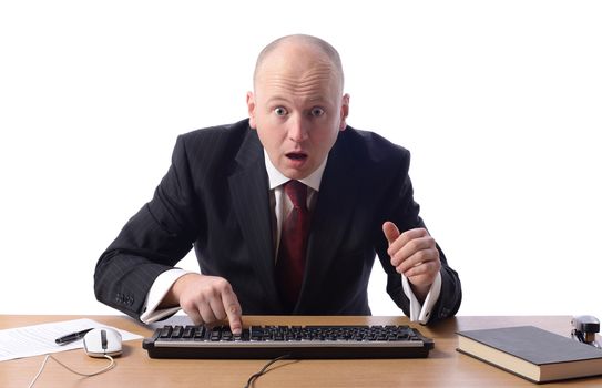 Surprised businessman sat at desk looking at computer screen isolated on white.
