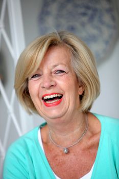 Laughing vivacious senior woman with short blond hair, head and shoulders portrait
