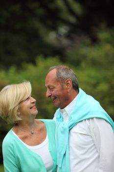 Happy romantic senior couple standing looking into each others eyes and smiling outdoors in a green park