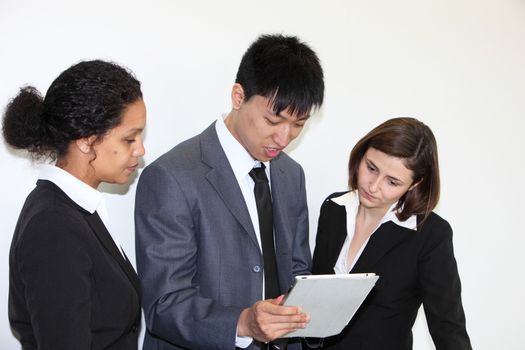 Three multiethnic young business colleaues consulting a tablet-pc held by an Asian businessman as they stand together in an office