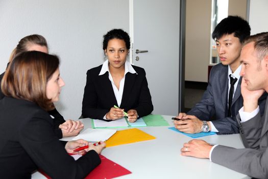 Group of multiethnic diverse young business people in a meeting sitting around a table with serious expressions discussing a new strategy or solution to a problem