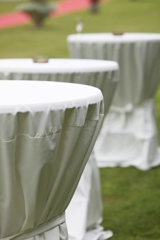 Three round tables wrapped in crispy white table clothes prepared for a special event outdoors