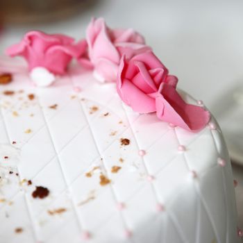 Pink icing roses on one tier of a wedding cake covered in white icing decorated with a geometric diamond pattern