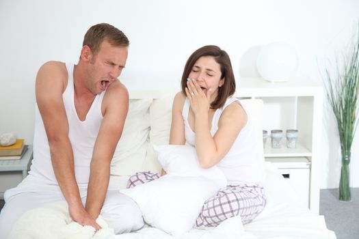 Middle-aged Caucasian sleepy couple yawning while sitting in bed in the bedroom