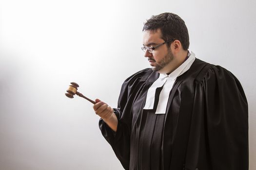 Overweight man in canadian lawyer toga, looking intensely at a gavel in his hand