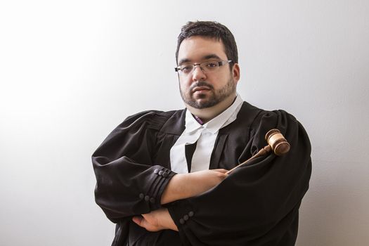 Overweight man in canadian lawyer toga, with arms cross, holding a gavel in his hand