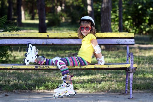 little girl with roller skates sitting on bench