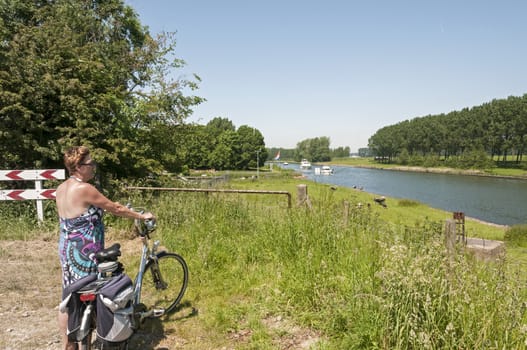 woman standing with bike looking at the boats going by on the river in Holland