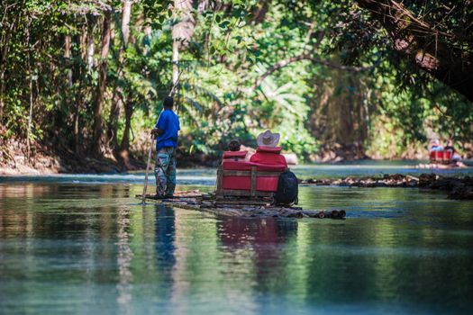 Two tourists with bamboo boat captain on river in Jamaica