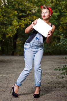 Beautiful pin-up girl in denim overalls and a red bandana holding copyspace