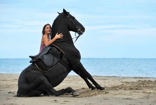 sitting black stallion on the beach with young woman