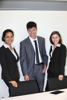 International young professional team made of one confident Asian businessman and two businesswomen smiling, wearing formal clothes while standing in the office