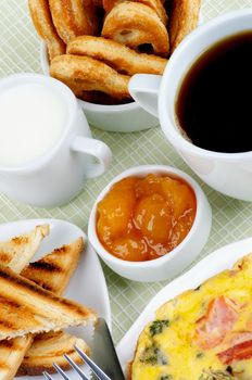 Delicious Hearty Breakfast with Omelet, Toasts, Apricot Jam, Coffee, Milk and Puff Pastry closeup on light green Checkered background