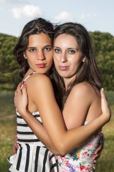 View of a two young women in tight and short dresses hugging in nature.