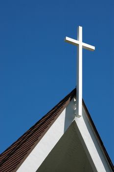A wooden cross on top of a church against a bright, blue sky