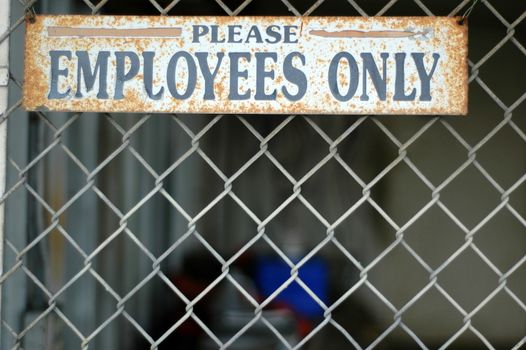 A Rusty 'Employees Only' Sign on a Chain Link Fence at an Abandoned Industrial Building