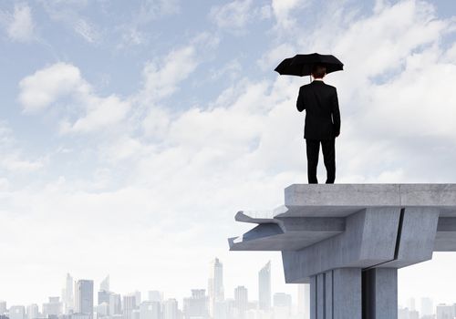 Image of businessman with umbrella standing at the edge of bridge