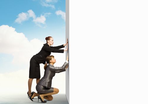 Two businesswoman pushing blank white banner. Place for text