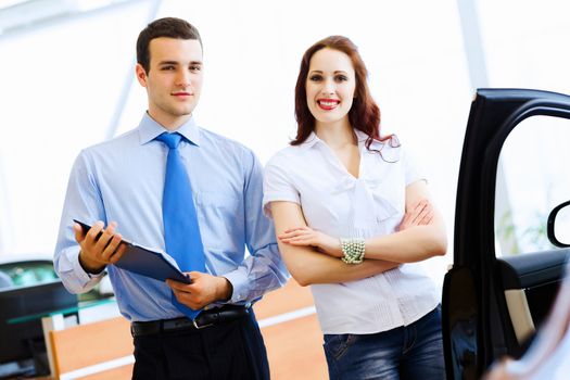 Attractive woman at car salon with consultant choosing a car