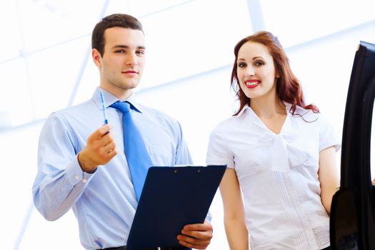 Attractive woman at car salon with consultant choosing a car