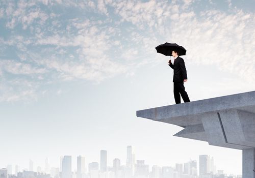 Image of businessman with umbrella standing at the edge of bridge