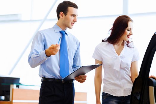 Attractive woman at car salon with consultant choosing a car