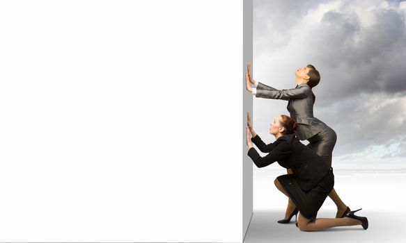 Image of two businesswomen pushing blank wall. Place for text