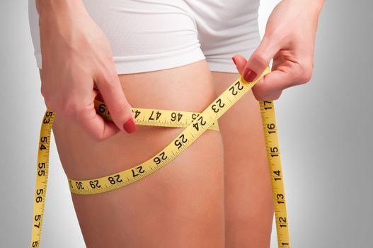 Woman measuring her thigh with a yellow measuring tape