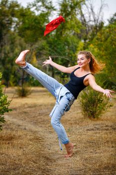 Beautiful pin-up girl barefoot in jeans overalls throws a red bandanna