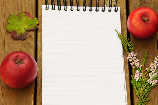 A notebook with a blank page with autumn theme, apples, heather and a leaf