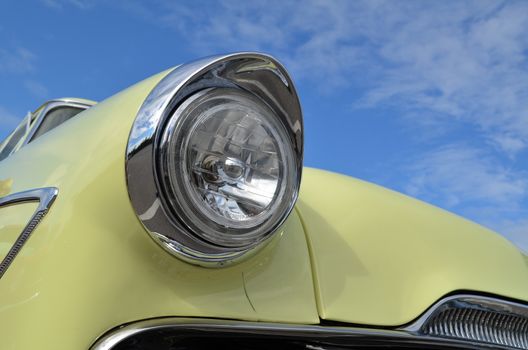 American classic car in bright yellow paint work showing its headlamp with chrome trim.