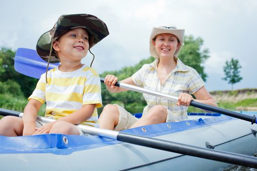 Happy young boy with mother paddling kayak on the river in lovely summer day