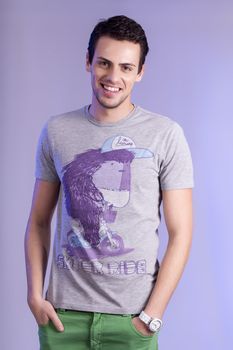 View of a young man standing against a purple  background. 