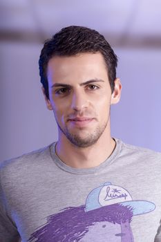 View of a young man standing against a purple  background. 