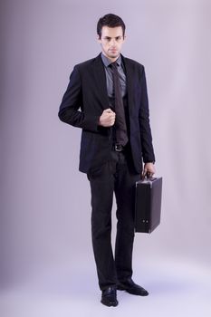 View of a young business man standing against a grey  background. 