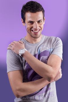 View of a young man standing against a purple  background. 