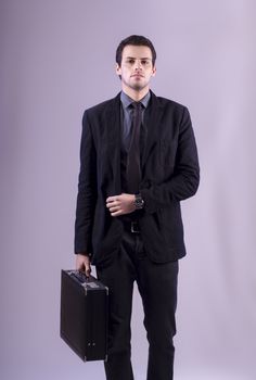 View of a young business man standing against a grey  background. 