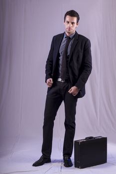 View of a young business man standing against a grey  background. 