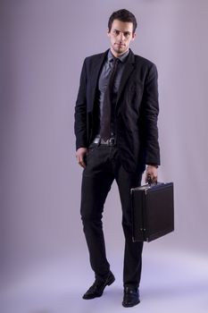 View of a young business man standing against a grey  background. 