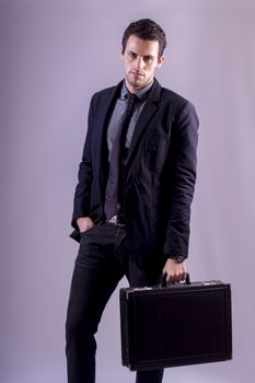 View of a young business man standing against a grey  background. 