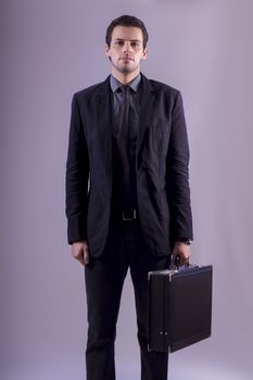 View of a young business man standing against a grey  background. 