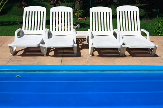 four white deckchair by the blue swimming pool